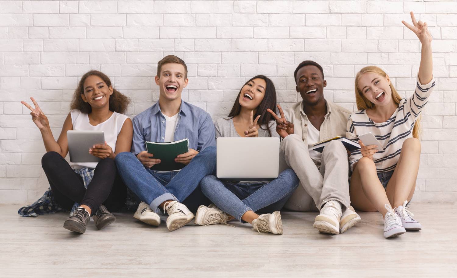 group of happy high school students sitting against a wall